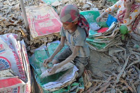 Téléchargez les photos : 19 décembre 2023 Sylhet-Bangladesh : Un jeune garçon avec sa mère qui travaille pour un revenu supplémentaire pour sa famille risque sa vie en travaillant dans la poussière des sacs de ciment près de la rivière Surma à Sylhet, Bangladesh - en image libre de droit
