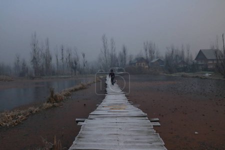 Téléchargez les photos : 21 décembre 2023, Srinagar Cachemire, Inde : Un homme marche sur un pont en bois recouvert de givre par un froid matin d'hiver à Srinagar. La période d'hiver la plus dure de 40 jours Chillai-Kalan, commence au Cachemire jeudi - en image libre de droit
