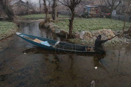 Téléchargez les photos : 21 décembre 2023, Srinagar Cachemire, Inde : Un homme conduit son bateau sur de l'eau partiellement gelée à l'intérieur du lac Dal à Srinagar. La période d'hiver la plus dure de 40 jours Chillai-Kalan, commence au Cachemire jeudi - en image libre de droit