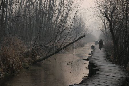 Téléchargez les photos : 21 décembre 2023, Srinagar Cachemire, Inde : Un homme marche sur un pont en bois recouvert de givre par un froid matin d'hiver à Srinagar. La période d'hiver la plus dure de 40 jours Chillai-Kalan, commence au Cachemire jeudi - en image libre de droit