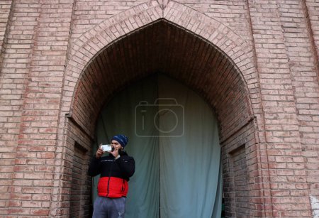 Téléchargez les photos : 12 janvier 2024, Srinagar Cachemire, Inde : Un homme prend des photos depuis son téléphone portable alors que les Cachemiris offrent des prières spéciales (pas sur la photo) dans le complexe de Jamia Masjid ou Grande Mosquée à Srinagar. Prières spéciales de la congrégation - en image libre de droit