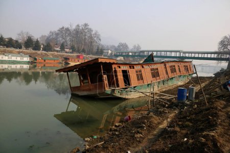 Photo for January 15,2024, Srinagar Kashmir, India : A capsized houseboat is seen on the banks of Jhelum river in Srinagar. Prolonged Dry Winter Spell Leaves Jhelum River at Historic Low, Jeopardizing Houseboats and Disappointing Skiers in Gulmarg. - Royalty Free Image