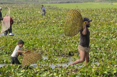 Foto de 15 enero 2024 - Bangladesh: Niños pescando con trampa de bambú en el Beel. Mientras que la gente rural armada con trampas de bambú y red de pesca hecha a mano para tomar parte en la celebración en un festival de pesca de polo bawa 100 años de invierno en el Gowahori - Imagen libre de derechos