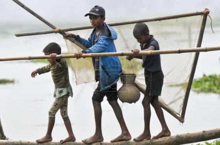 Téléchargez les photos : 15 janvier 2024 - Bangladesh : Des enfants pêchent avec un piège à poisson en bambou à la Beel. Alors que les ruraux armés de pièges à poisson en bambou et d'un filet de pêche fait à la main pour prendre part à la célébration d'un festival de pêche hivernal de polo bawa de 100 ans au Gowahori - en image libre de droit