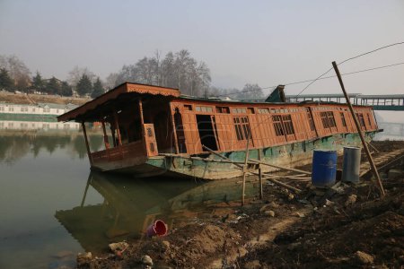 Photo for January 15,2024, Srinagar Kashmir, India : A capsized houseboat is seen on the banks of Jhelum river in Srinagar. Prolonged Dry Winter Spell Leaves Jhelum River at Historic Low, Jeopardizing Houseboats and Disappointing Skiers in Gulmarg. - Royalty Free Image
