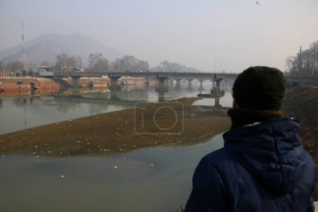 Téléchargez les photos : 15 janvier 2024, Srinagar Cachemire, Inde : Un homme regarde la partie sèche de la rivière Jhelum à Srinagar. Le charme prolongé de l'hiver sec laisse la rivière Jhelum à son plus bas niveau historique, Jeopardifie les péniches et déçoit les skieurs à Gulmarg - en image libre de droit