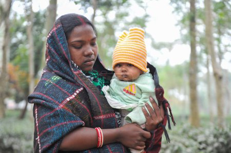Téléchargez les photos : 17 janvier 2024 Sylhet-Bangladesh : Un tout-petit sur les genoux d'un gardien dans la matinée froide dans les locaux du Tarapur Tea Garden. Les enfants et les personnes âgées souffrent de la sévérité croissante de l'hiver à Sylhet. - en image libre de droit