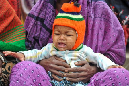 Foto de 17 enero 2024 Sylhet-Bangladesh: Un niño pequeño en el regazo del guardián en la fría mañana en las instalaciones del Tarapur Tea Garden. Niños y ancianos están sufriendo debido a la creciente severidad del invierno en Sylhet. - Imagen libre de derechos