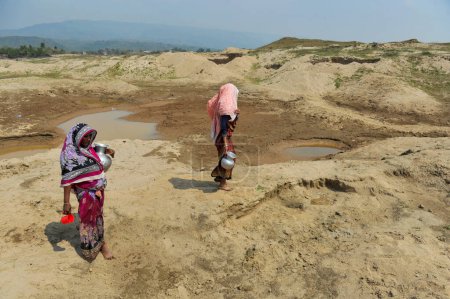 Foto de 5 de marzo de 2024, Sylhet, Bangladesh: Dos amas de casa están recolectando agua para uso doméstico de un depósito casi seco en el área de Kalairag de Bholaganj que bordea Companiganj upazila - Imagen libre de derechos