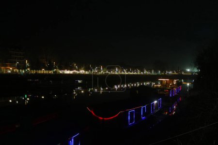 05. März 2024, Srinagar, Indien: Ein beleuchtetes Hausboot wird abends in Srinagar über den Fluss Jhelum gesehen