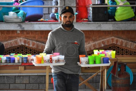 Téléchargez les photos : 19 mars 2024, Srinagar, Inde : Un homme porte des verres de lait devant une mosquée pendant le mois sacré du Ramadan - en image libre de droit