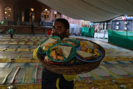 Téléchargez les photos : 19 mars 2024, Srinagar, Inde : Un homme porte un panier avec de la nourriture chargée devant une mosquée pendant le mois sacré du Ramadan - en image libre de droit