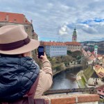 Female tourist in a hat, taking photos of Cesky Krumlov with her mobile phone. An old fairy tale town. Magical atmosphere and magnificent sky. High quality photo. 