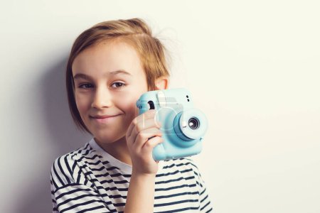 Téléchargez les photos : Cute boy holding photo camera. Stylish kid posing over grey background. Child with fun emotion and expreshion. Fashion and technology. - en image libre de droit