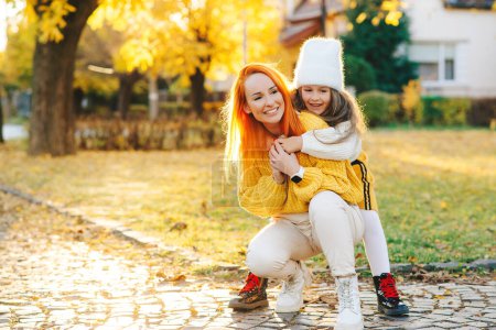 Foto de Mom and girl laughing outdoors. Autumn fashion. Happy family having fun together. Happy mother and daughter walking in the autumn park. Woman and child daughter playing outdoors. - Imagen libre de derechos