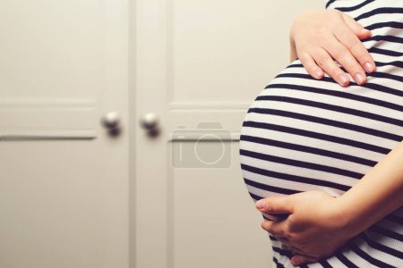 Téléchargez les photos : Pregnant woman's belly. Baby expectation. Pregnancy, maternity, preparation and expectation concept. Woman dreaming about child. Background with copy space. Pregnant woman holdig hands on belly, closeup. - en image libre de droit