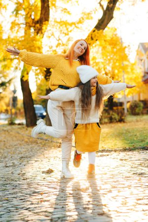 Téléchargez les photos : Happy family enjoying the autumn vacation at nature. Stylish family on autumn walk. Mother and daughter walking in the park. Mom and child having fun together. Autumn fashion, lifestyle and vacation. - en image libre de droit