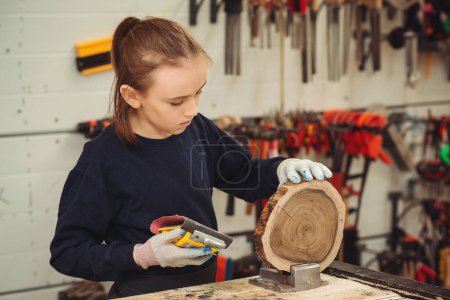 Photo for Young carpenter working with wood and sandpaper in craft workshop. School, development and learning concept. Cute boy makes wooden clock in the workshop. - Royalty Free Image