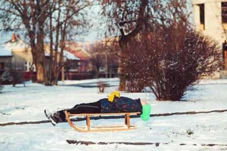 Photo for Boy with broken hand outdoors in winter park. Cute kid with broken arm and gypsum sitting on sled. Mischievous child with a cast. - Royalty Free Image