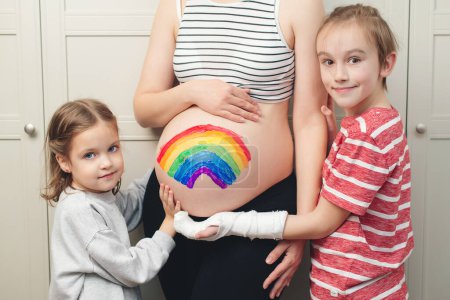 Photo for Cute boy with sister drawing rainbow on pregnant belly their mother. Baby birth expecting time and belly painting. Happy children and pregnant mom having fun together at home. - Royalty Free Image