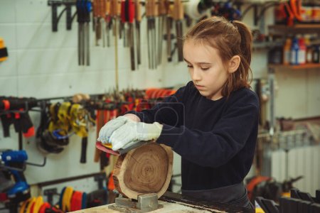 Photo for Cute boy makes wooden clock in the workshop. Young carpenter working with wood and sandpaper in craft workshop. School, development and learning concept. - Royalty Free Image