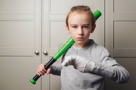 Téléchargez les photos : Kid with broken hand after training. Sport time and healthcare. Health, lifestyle and sport concept. Boy with a broken arm in plaster holding baseball bat. - en image libre de droit