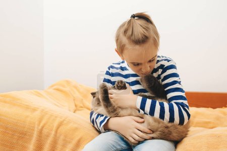 Foto de Cute boy plays with a cat at home. Happy kid hugging his cat. Boy relaxing on the bed with pet. Childhood, true friendship and home pet. - Imagen libre de derechos