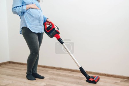 Photo for Easy cleaning with a wireless vacuum cleaner. Pregnant woman cleaning floor with handheld vacuum cleaner. Young pregnant woman enjoys cleaning her house. Modern easy cleaning. - Royalty Free Image