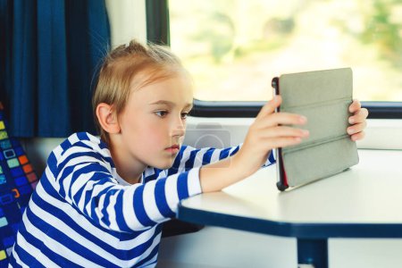 Photo for Cute child playing video games online on tablet during trip. Kid travels on a train. Childhood, family vacation, lifestyle. Journey. Gadget addiction. - Royalty Free Image