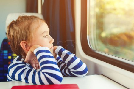 Photo for Little boy is traveling on the train. Kid travels on a train. Cute child looking out the train window. Childhood, family vacation, lifestyle. - Royalty Free Image