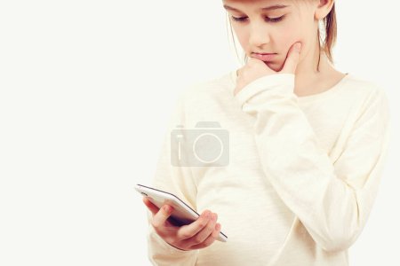 Photo for Smart kid holding a mobile phone. Technology, lifestyle and people concept. Cute boy using a smart phone over white background. Pensive young boy with a serious face thinking about a question. - Royalty Free Image