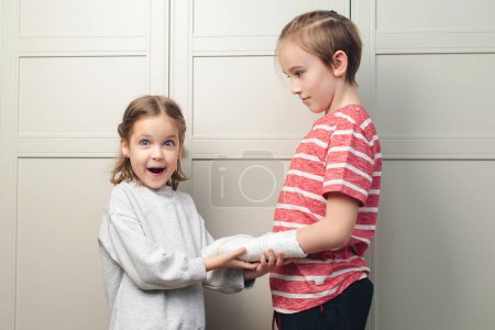 Photo for Child girl holding his brother's broken arm. Boy holds hand bent broken arm cast on his arm. Girl is in shock - Royalty Free Image