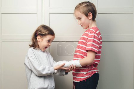 Photo for Boy two broken arms, girl is in shock. Shocked surprised boy with arm in sling. Boy has a cast on his arm. Child girl holding his brother's broken arm. Boy holds hand bent broken arm cast on his arm. - Royalty Free Image