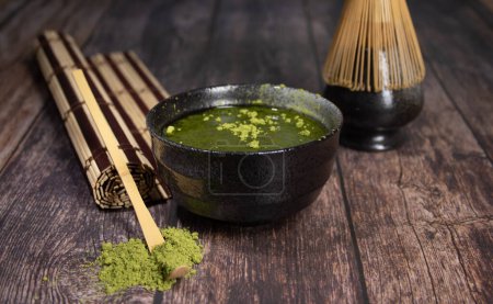 Photo for Tea matcha black bowl with gray stains whisk and bamboo spoon on wooden table with tea green powder on top and a rolled cane tablecloth photo of diner close-up with space for text - Royalty Free Image