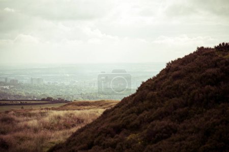 Photo for A large dark hill half-blocks the view of a city that is somewhat lost in the haze - Royalty Free Image