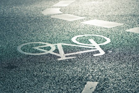 Photo for In the centre of the picture you can see the bicycle symbol of a white road marking, which stands out brightly against the asphalt due to the low sun - Royalty Free Image