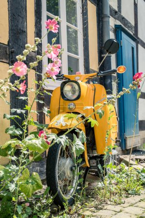 Photo for In front of a half-timbered house is a yellow scooter overgrown with flowers - Royalty Free Image