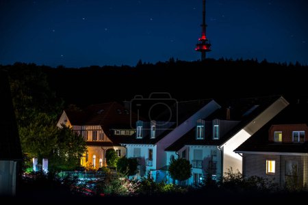 Photo for Illuminated row of houses of a residential area at night, in the background the forest slope with television tower - Royalty Free Image