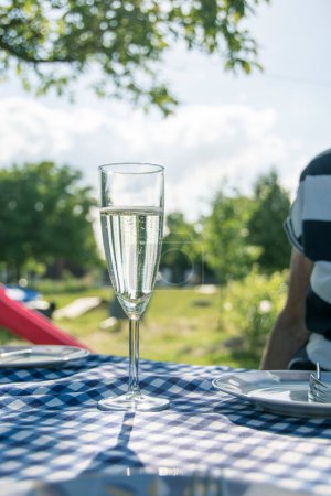 Photo for On a table with a blue-checked tablecloth, there is a glass of champagne to celebrate the day. - Royalty Free Image