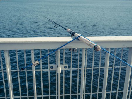 Photo for A fishing rod is attached to a bridge handrail over a lake. - Royalty Free Image