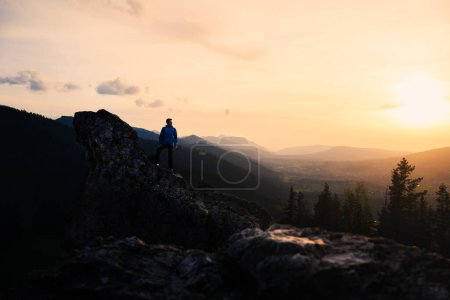 Téléchargez les photos : Au crépuscule, une personne se tient sur un sommet de montagne, entouré par le paysage naturel. Le ciel est peint avec des couleurs vives du coucher du soleil - en image libre de droit