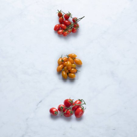 Foto de Tomates de Italia, aislados sobre fondo de mármol Ramo de tomates cherry italianos, naranja o variedad amarilla, con rama, ramita, tres grupos de primer plano Macro, vista superior, desde arriba - Imagen libre de derechos