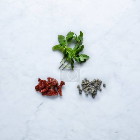 Photo for Aromatic Flavoring, Isolated on Marble Background  Dried Tomatoes from Italy, Salted Capers Bunch, Mint Bundled with Twine on Stone Kitchen Table  Detailed Close-Up Macro, High Resolution, Top View - Royalty Free Image