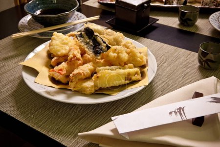 Téléchargez les photos : Tempura dans une assiette de restaurant japonais avec légumes et crevettes frites en pâte, baguettes, assiettes en céramique, dîner gastronomique sur table en bois noir et napperons haute résolution Fermer - en image libre de droit