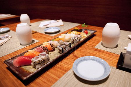 Foto de Sushi en plato de restaurante de comida japonesa con salsa de soja, palillos, hilera de nigiri y rollos con Wasabi, caviar rojo, cena gourmet en mesa de madera y manteles detallados, primer plano de alta resolución - Imagen libre de derechos