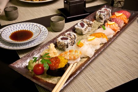 Téléchargez les photos : Sushi dans une assiette de restaurant japonais avec sauce soja, baguettes, rangée de nigiris et rouleaux avec wasabi, caviar rouge, dîner gastronomique sur table noire et napperons Détail, haute résolution Gros plan - en image libre de droit