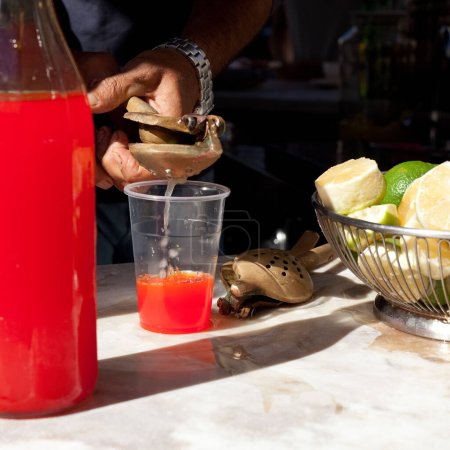 Photo for Seltzer Soda Drink in Sicily ("Selz")  Traditional Italian Kiosk Background with Red Mandarin Drink and Lemons on Marble  Close-Up Macro on Bartender Pouring Soda Water on Plastic Cup, with Squeezer - Royalty Free Image