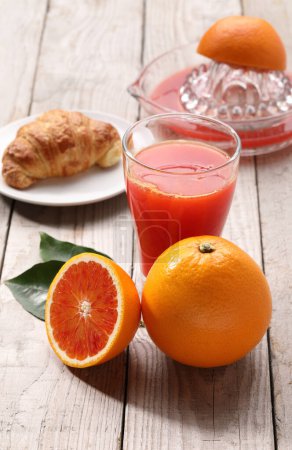 Téléchargez les photos : Boisson de jus d'orange en verre sur une table en bois blanche Oranges entières, feuilles vertes, avec ombres, jus rouge Photo d'ingrédient minimaliste de haute qualité - en image libre de droit