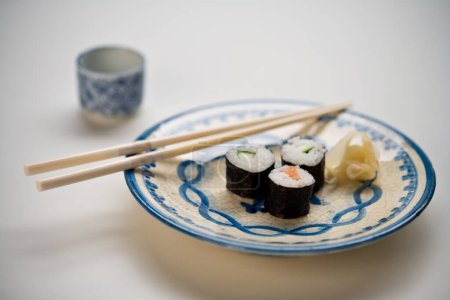 Foto de Placa con sushi Maki, jengibre, palillos y un tazón de sake - Imagen libre de derechos