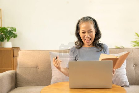 Photo for Happy old woman working on her laptop at home. Staying at home. Working from home. Happy middle aged senior woman sitting at desk at home working using laptop computer. - Royalty Free Image